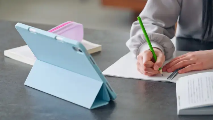 Uczeń pisze w zeszycie, korzystając z tabletu. Tak właśnie płaci się za nauczanie indywidualne w erze cyfrowej.