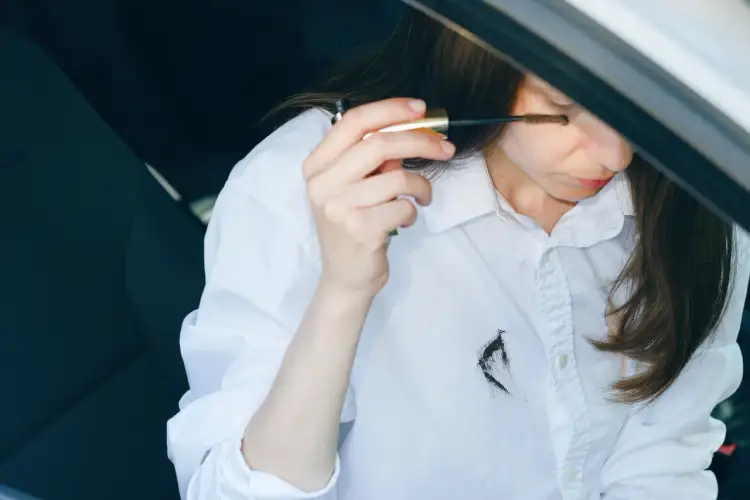 Kobieta w białej koszuli próbuje nałożyć tusz do rzęs, ale przypadkowo ubrudziła koszulę.