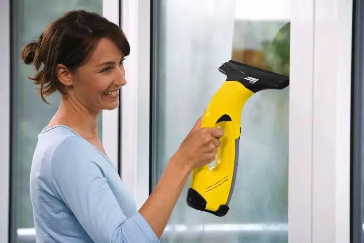 Kobieta z uśmiechem czyści okno żółtą myjką Karcher. Czy myjka do okien Karcher zostawia smugi przez zużyte gumy czy zły płyn?