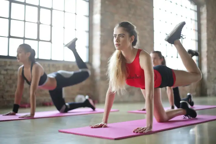 Kobiety ćwiczą pilates, co daje im siłę i elastyczność. W tle duże okna i ceglana ściana.
