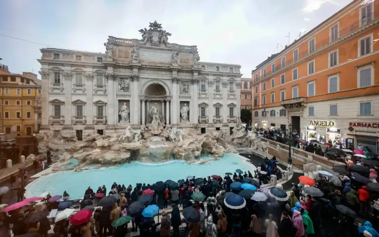 Tłum turystów z parasolami podziwia Fontannę di Trevi na Piazza di Trevi w Rzymie, Włochy.