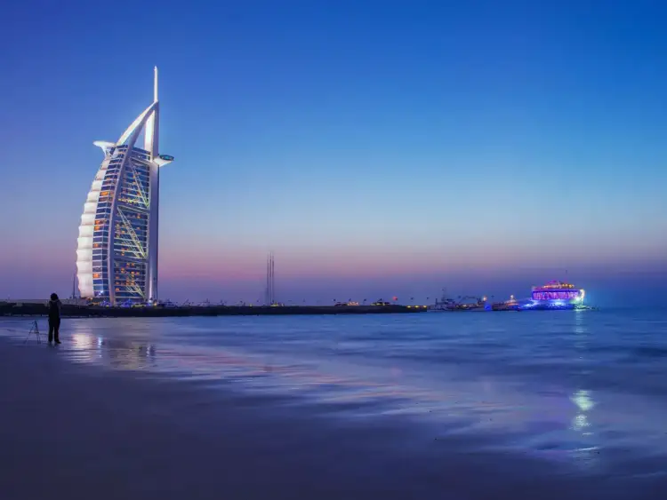 Zachód słońca w Dubaju, z luksusowym hotelem Burj Al Arab i oświetloną łodzią. Zastanawiasz się, ile kosztuje wycieczka do Dubaju?