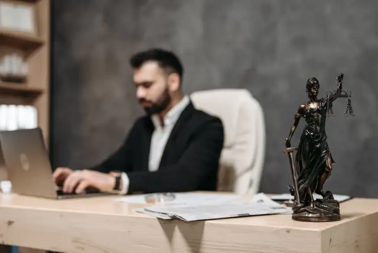 Mężczyzna w garniturze pracuje przy laptopie. Obok statua Temidy. Kto umawia notariusza sprzedający czy kupujący?