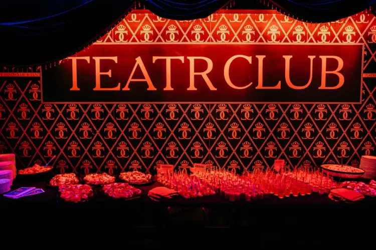 Elegancka ściana z napisem TEATR CLUB i wzorem koron. Na pierwszym planie stół z przekąskami i kieliszkami.