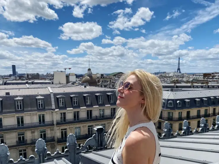 Kobieta na tarasie widokowym Galerii Lafayette podziwia panoramę Paryża z Wieżą Eiffla w tle.