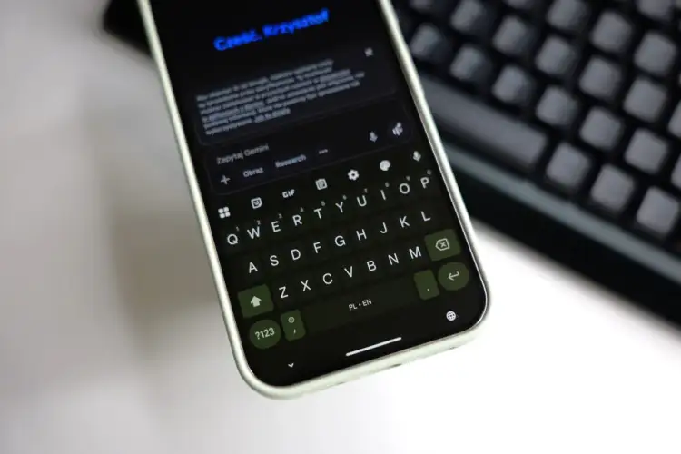 Klawiatura Gboard na telefonie wyświetla zapytanie do Gemini. Widoczny jest też fragment klawiatury fizycznej.