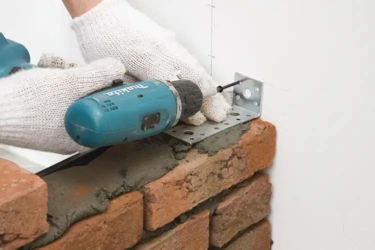 Rękawice i wiertarka pomagają w murowaniu ścianek działowych, mocując metalowy kątownik do ściany.