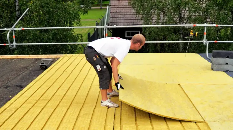 Pracownik układa płyty izolacyjne na dachu płaskim.