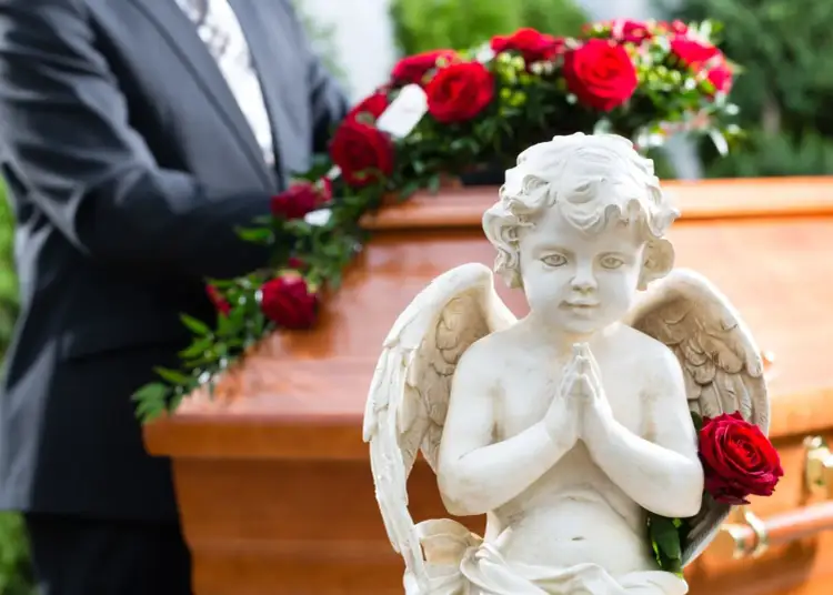 Aniołek z różą obok trumny, symbolizujący obrzędy pogrzebu. W tle mężczyzna w garniturze.