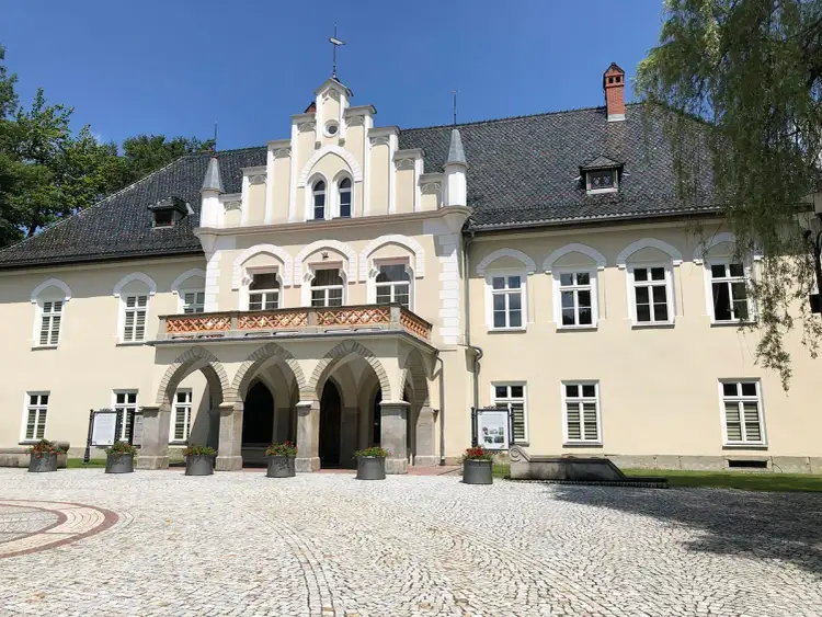 Elegancki dwór w Łodygowicach z arkadowym podcieniem i ozdobną balustradą, otoczony brukowanym dziedzińcem.