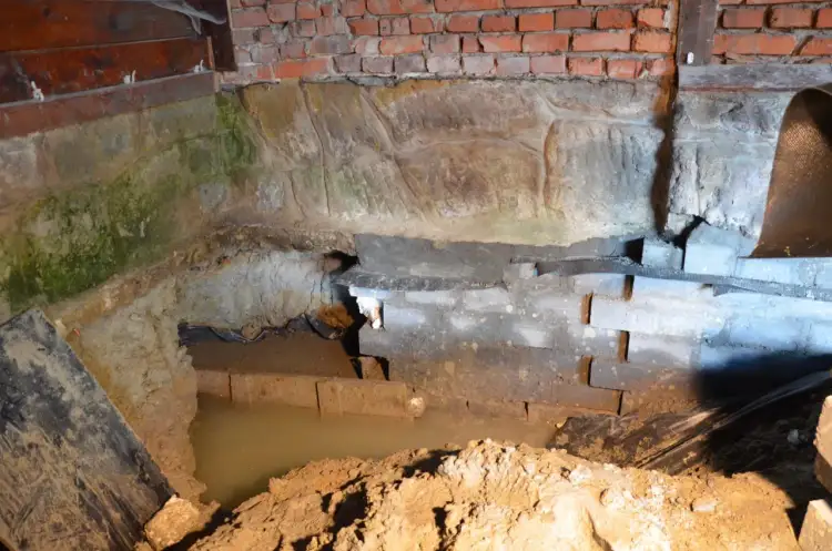 Prace przy hydroizolacji fundamentów od wewnątrz. Widoczny wykop, wilgoć i elementy konstrukcyjne.