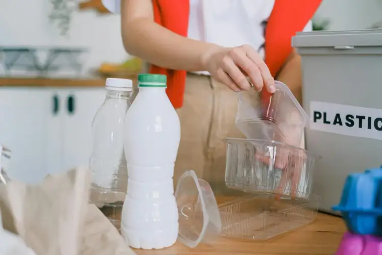 Segregacja odpadów to pierwszy krok, jak ograniczyć plastik. Ręka wrzuca plastikowe opakowania do pojemnika z napisem "PLASTIC".