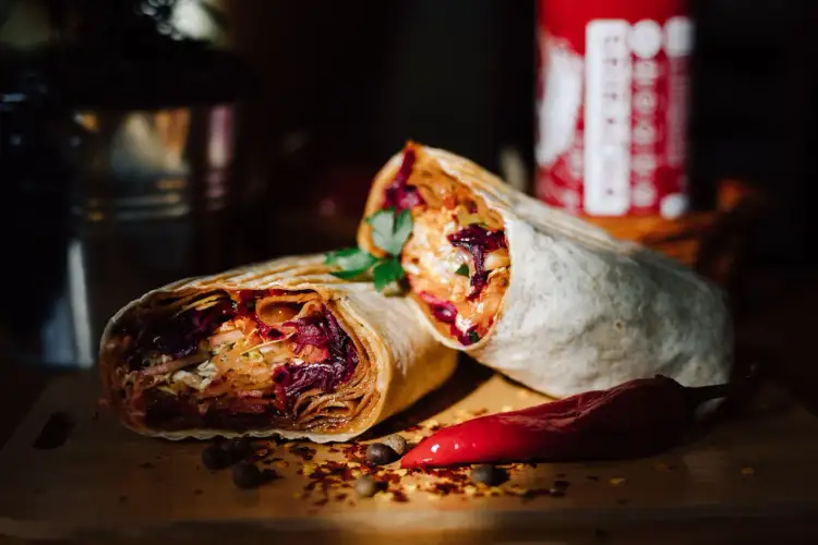 Dwa soczyste rolady efez doner kebab, pełne warzyw i mięsa, leżą obok czerwonej papryczki chili.