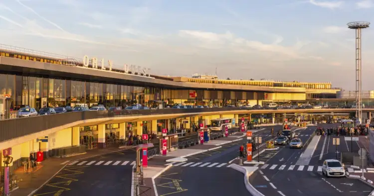 Port lotniczy Paryż-Orly Ouest w złotym świetle zachodzącego słońca. Samochody i autokary czekają na pasażerów.