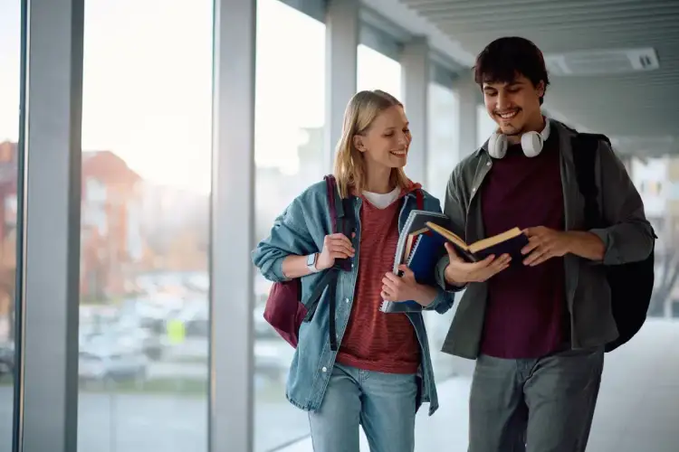 Dwóch studentów rozmawia o książce, idąc korytarzem. To może być przykład tego, co to jest wykształcenie średnie branżowe – praktyczna wiedza zdobywana w szkole.