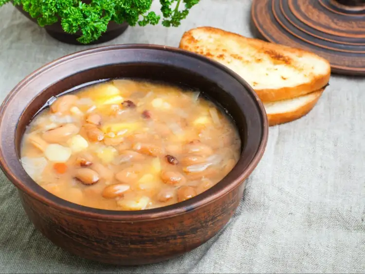 Gęsta, sycąca zupa fasolowa w glinianej misce, obok grzanki. Czy zupa fasolowa jest zdrowa? Tak, to bogactwo białka i błonnika!