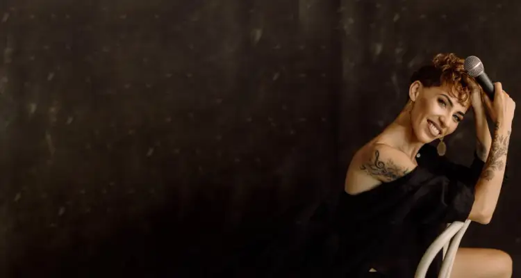 Uśmiechnięta kobieta z tatuażami trzyma mikrofon, gotowa do śpiewania. Idealna do aplikacji do nauki śpiewu.