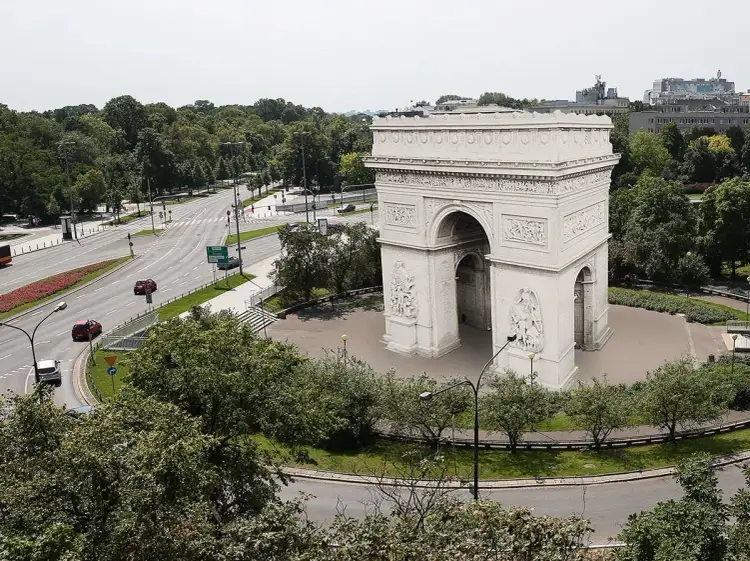 Łuk Triumfalny w Warszawie, otoczony zielenią i ruchem miejskim, przypomina o historii i architekturze miasta.