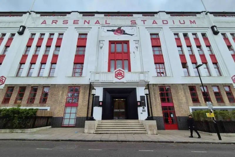 Dawny stadion Arsenalu w Highbury, z charakterystycznym napisem "ARSENAL STADIUM" i czerwonymi akcentami.