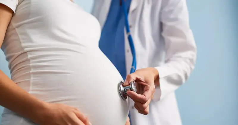 Lekarz osłuchuje brzuch ciężarnej kobiety stetoskopem. Dbałość o zdrowie w ciąży to podstawa.