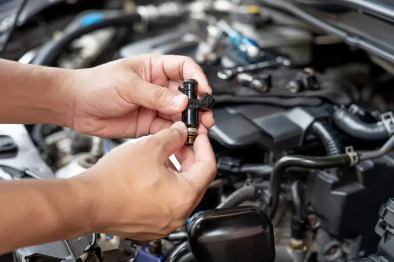 Mani che tengono un iniettore, componente essenziale per il corretto funzionamento del motore.
