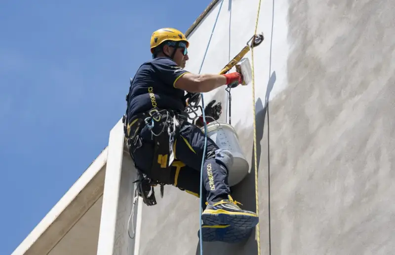Trabajador en altura realiza instalación SATE, aplicando revestimiento en fachada con equipo de seguridad.
