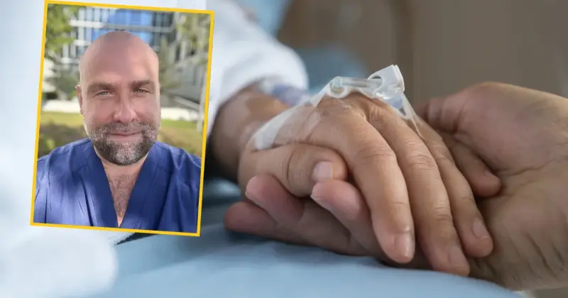Uśmiechnięty mężczyzna w niebieskim uniformie medycznym podaje słowa otuchy choremu na raka, trzymając go za rękę z wenflonem.
