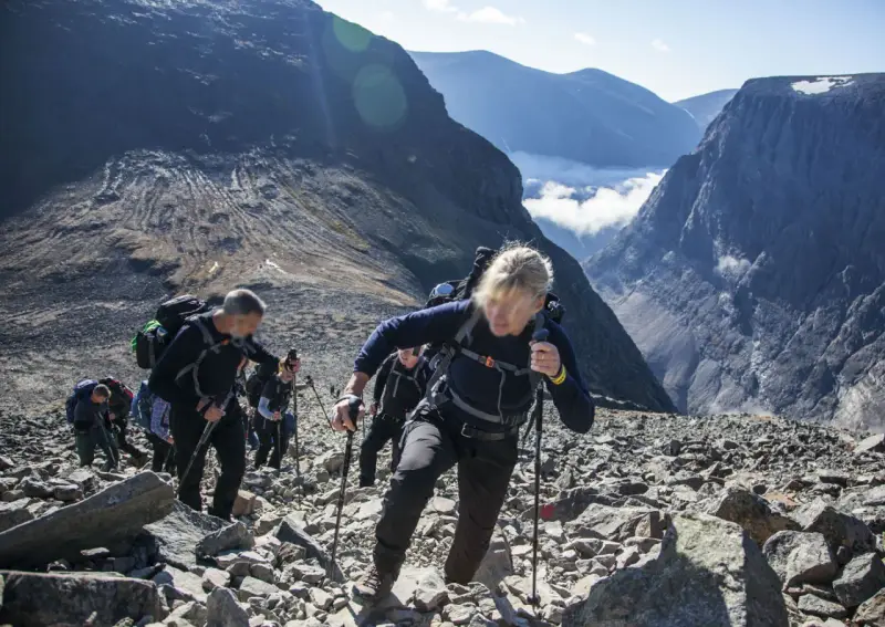 Vandring uppför stenigt landskap mot Sveriges högsta berg. Moln och bergstoppar i bakgrunden.
