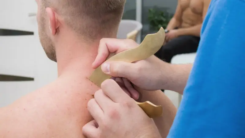 Masaż karku z użyciem narzędzi do pinoterapii. Terapeuta wykonuje zabieg na skórze pacjenta.