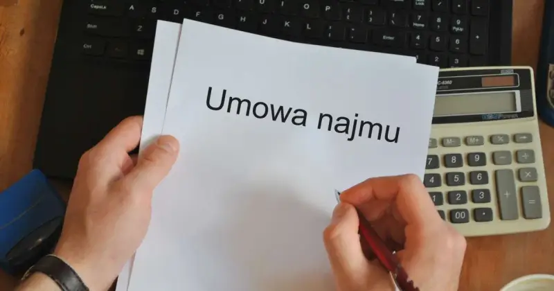 Ręka pisze długopisem na umowie najmu, obok kalkulator i laptop. Czas pomyśleć o podatku od najmu.