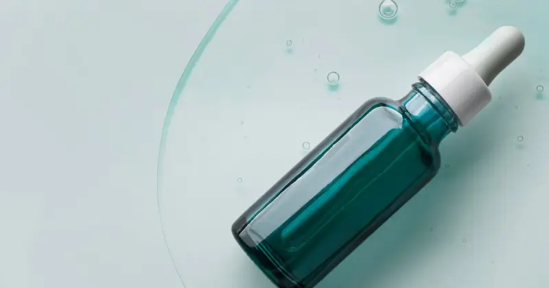 Szklana buteleczka z pipetką, wypełniona zielonym serum, na tle płynu z bąbelkami.