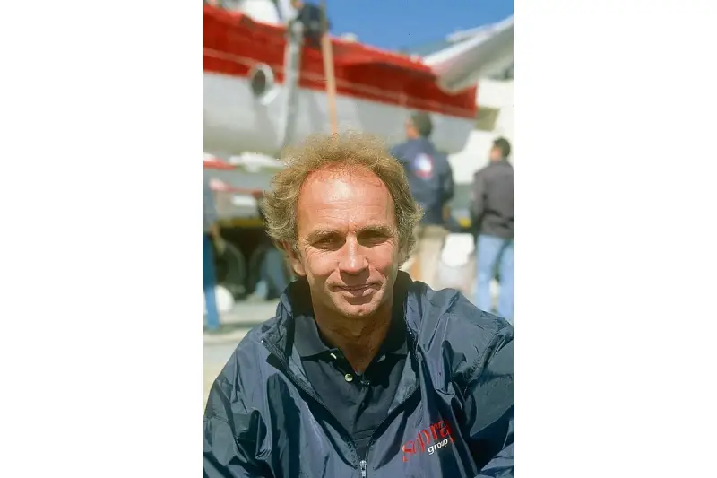 Jean-Claude Parisis, navigateur, souriant devant un avion rouge et blanc.