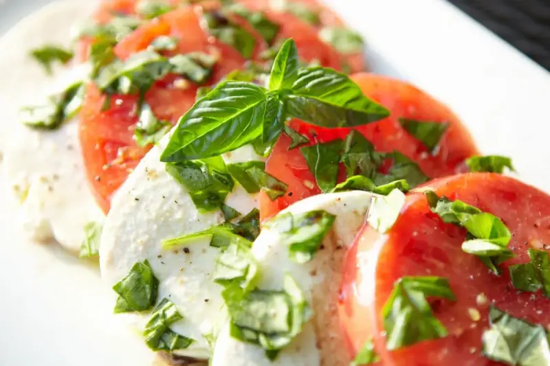 Salade Caprese : fines tranches de tomates rouges et de mozzarella crémeuse, parsemées de basilic frais. Une recette simple et savoureuse.