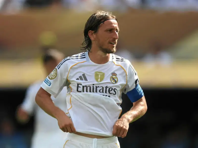 Luka Modrić w białej koszulce Realu Madryt, gdzie gra, z opaską na ramieniu.