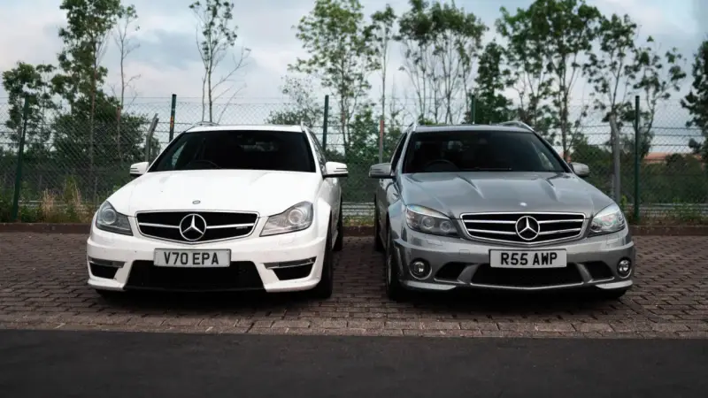 Dwa Mercedesy C63 AMG W204, biały i szary, stoją obok siebie na parkingu.