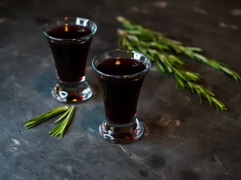 Dwa kieliszki ciemnego, aromatycznego nalewki z czernic, ozdobione gałązkami rozmarynu.