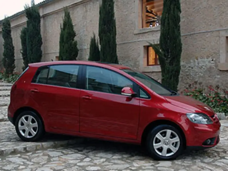 Roter VW Golf Plus mit Automatikgetriebe, der vor einem Steingebäude parkt. Mögliche Probleme mit dem Automatikgetriebe sind ein Thema.