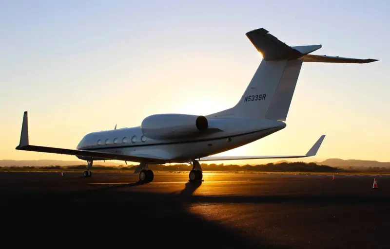 Ein weißer Privatjet steht im Sonnenuntergang auf dem Rollfeld. Verschiedene privatjets modelle sind auf dem Markt, aber dieser hier strahlt Luxus aus.