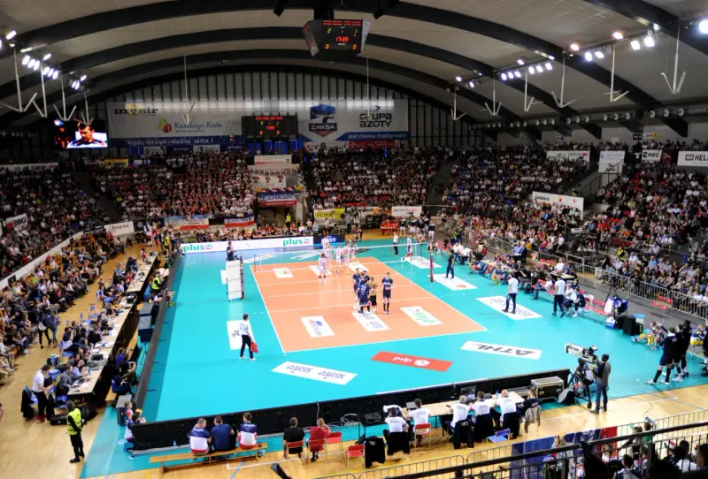 Widownia kibicuje podczas meczu siatkówki ZAKSA. Pełna hala, zawodnicy na boisku, emocje sięgają zenitu.
