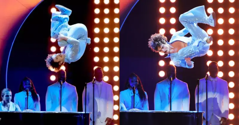 Wokalista w błyszczącym niebieskim stroju wykonuje akrobacje na scenie podczas gali nagród Grammy. Laureaci nagród grammy w białych garniturach stoją za fortepianami.