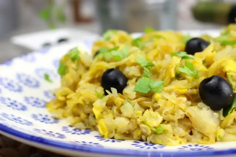 Delicioso bacalao a bras, un plato tradicional con patatas finas, huevo y aceitunas negras, adornado con perejil fresco.