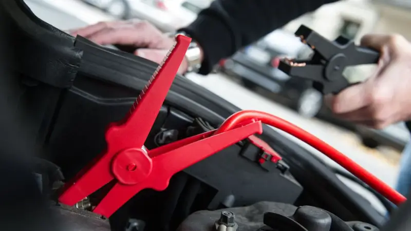 Rotes Kabel mit Krokodilklemme wird an Autobatterie angeschlossen. Plus oder Minus?