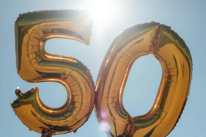 Gyllene ballonger formar siffran 50 mot en klarblå himmel. Perfekt för roliga frågor till 50 års fest!