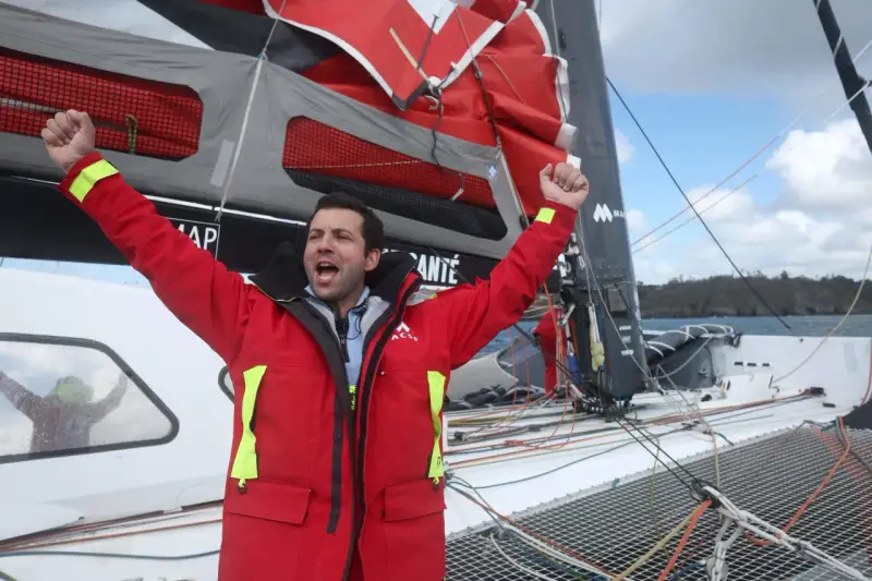 Un marinier en veste rouge célèbre sur un voilier. Une opportunité unique : ce voilier est à donner gratuitement !