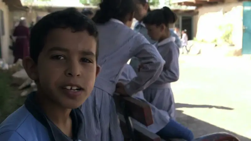Un garçon souriant pose devant des filles en uniforme dans la même cour d'école.