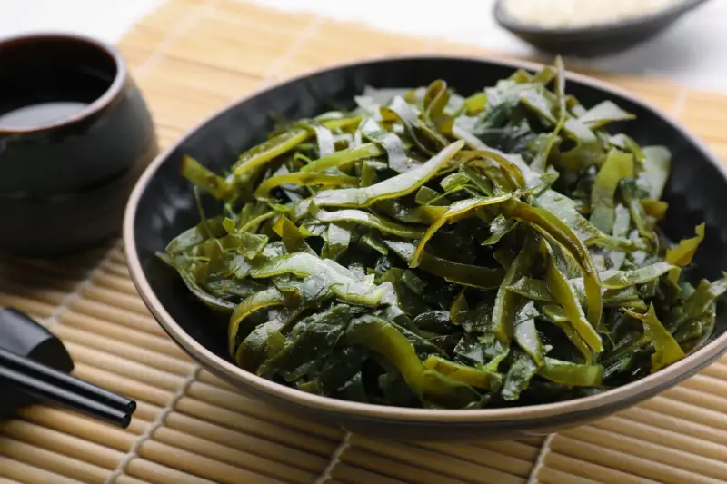 Un bol de salade d'algues kombu, aux multiples algue kombu bienfaits, servi avec une sauce et des baguettes sur un tapis de bambou.