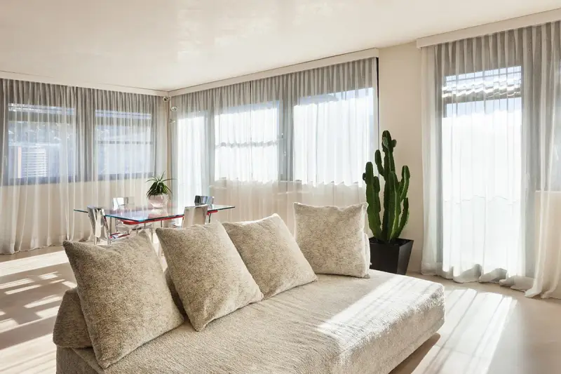 Soggiorno luminoso con divano beige e tende che non fanno vedere dall'esterno, creando un'atmosfera intima.