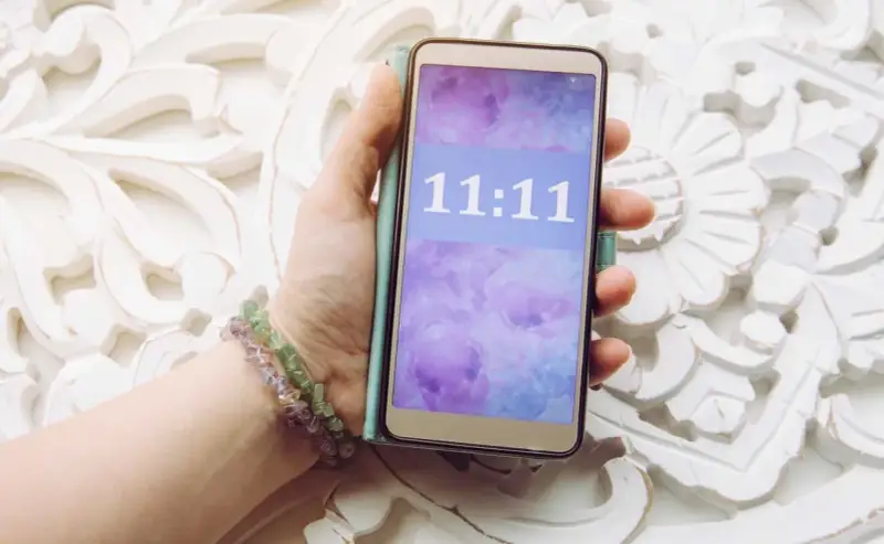 Dłoń trzyma telefon z wyświetloną godziną 11:11, co może mieć szczególne znaczenie.