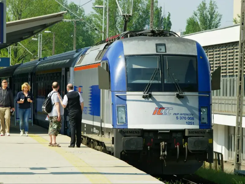 Pasażerowie czekają na pociąg PKP Intercity, gotowi do podróży z biletem wakacyjnym.