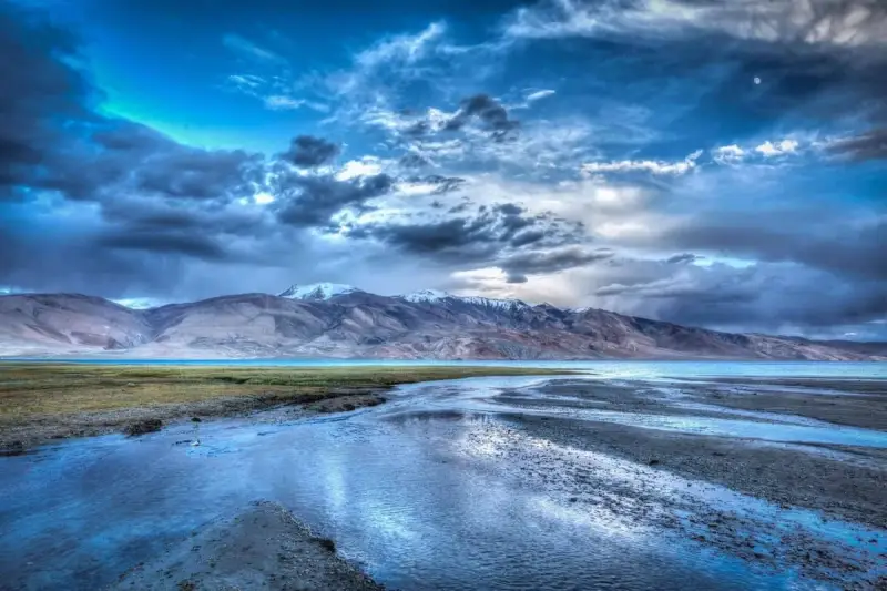 Paesaggio montano con lago e fiume, cielo drammatico con nuvole scure e luna, effetto HDR.